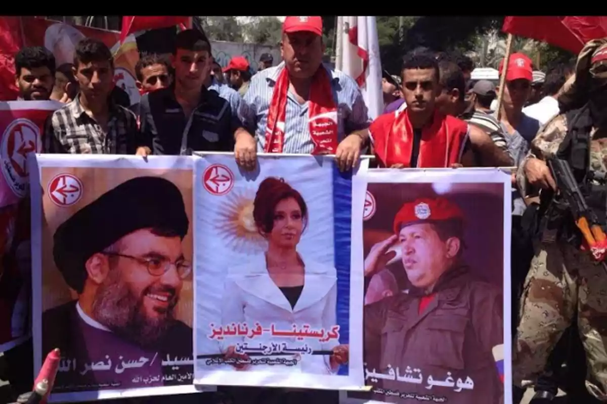 Grupo de personas manifestándose y sosteniendo pancartas con imágenes de líderes políticos y banderas rojas
