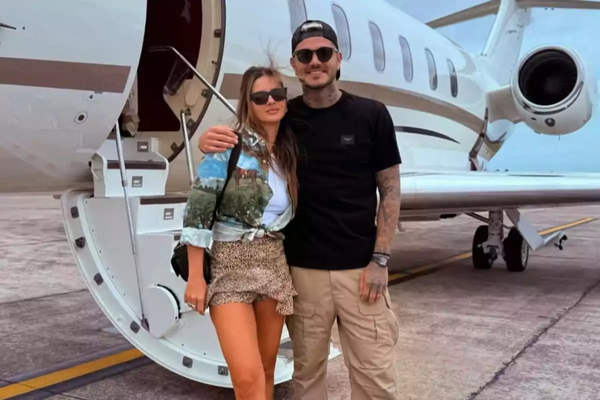 Una pareja posando frente a un jet privado en una pista de aterrizaje.