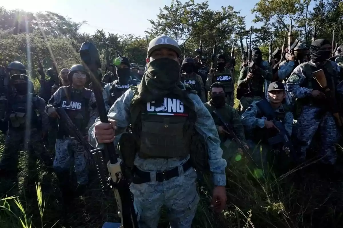 Un grupo de personas armadas con uniformes y pasamontañas en un entorno al aire libre.