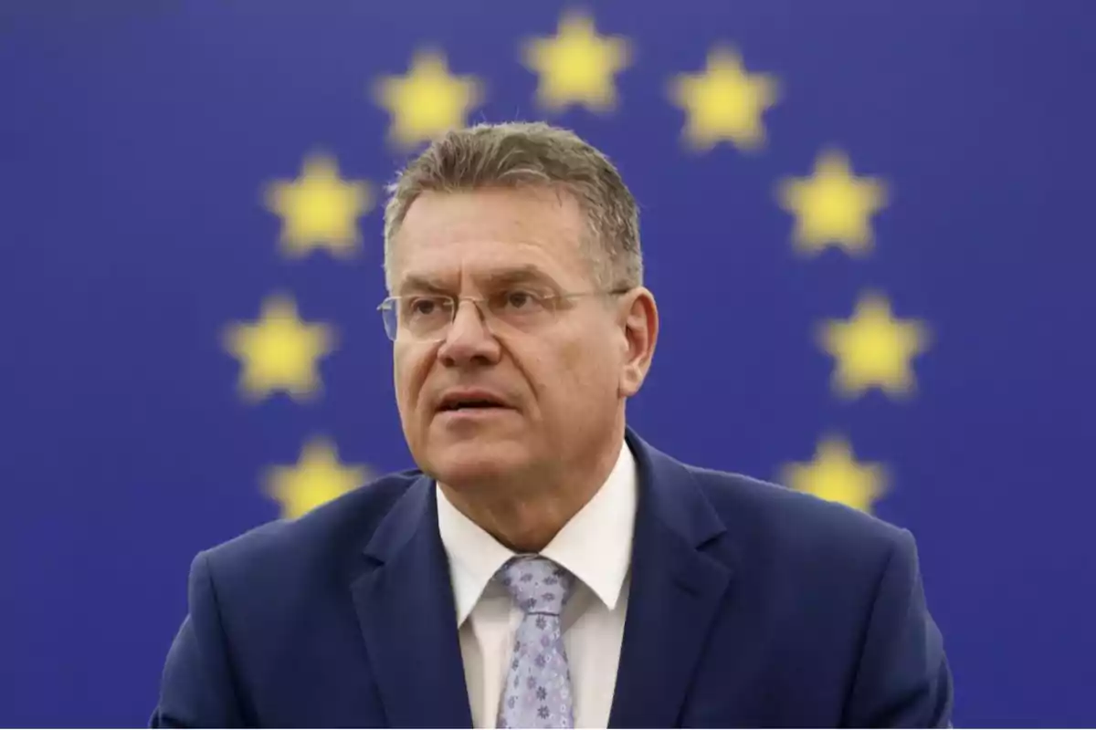 Hombre con traje y corbata frente a una bandera de la Unión Europea. Hombre con traje y corbata frente a una bandera de la Unión Europea.