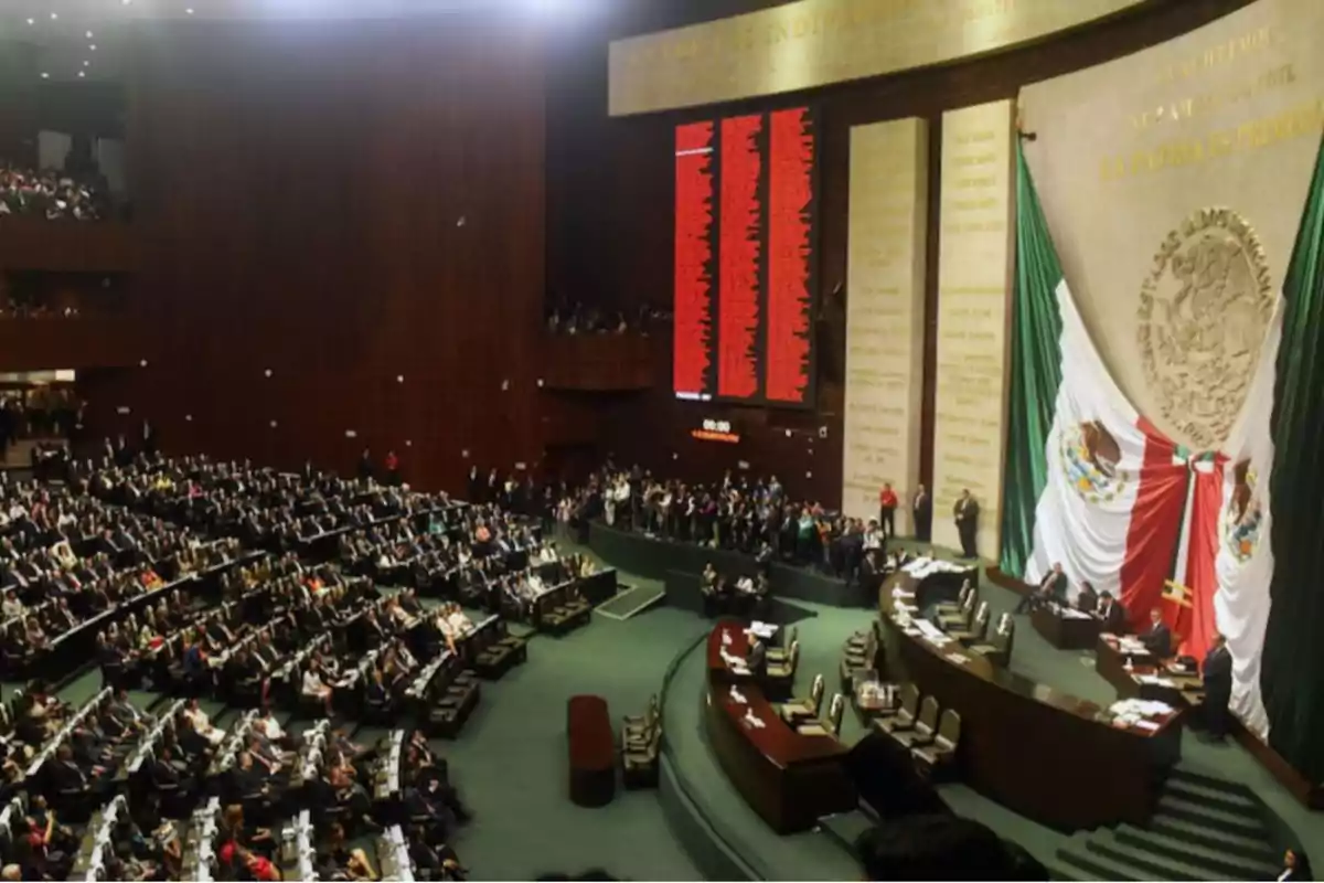A session inside a parliament with numerous attendees seated, a large national emblem, and a flag on the wall. A session inside a parliament with numerous attendees seated, a large national emblem, and a flag on the wall.