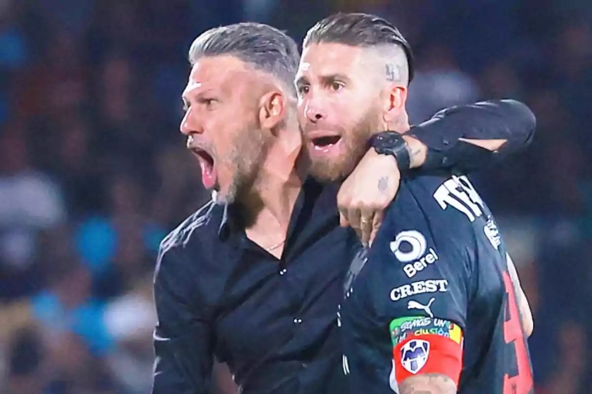 Dos hombres celebran efusivamente en un partido de fútbol uno de ellos lleva un uniforme deportivo y un brazalete de capitán Dos hombres celebran efusivamente en un partido de fútbol uno de ellos lleva un uniforme deportivo y un brazalete de capitán