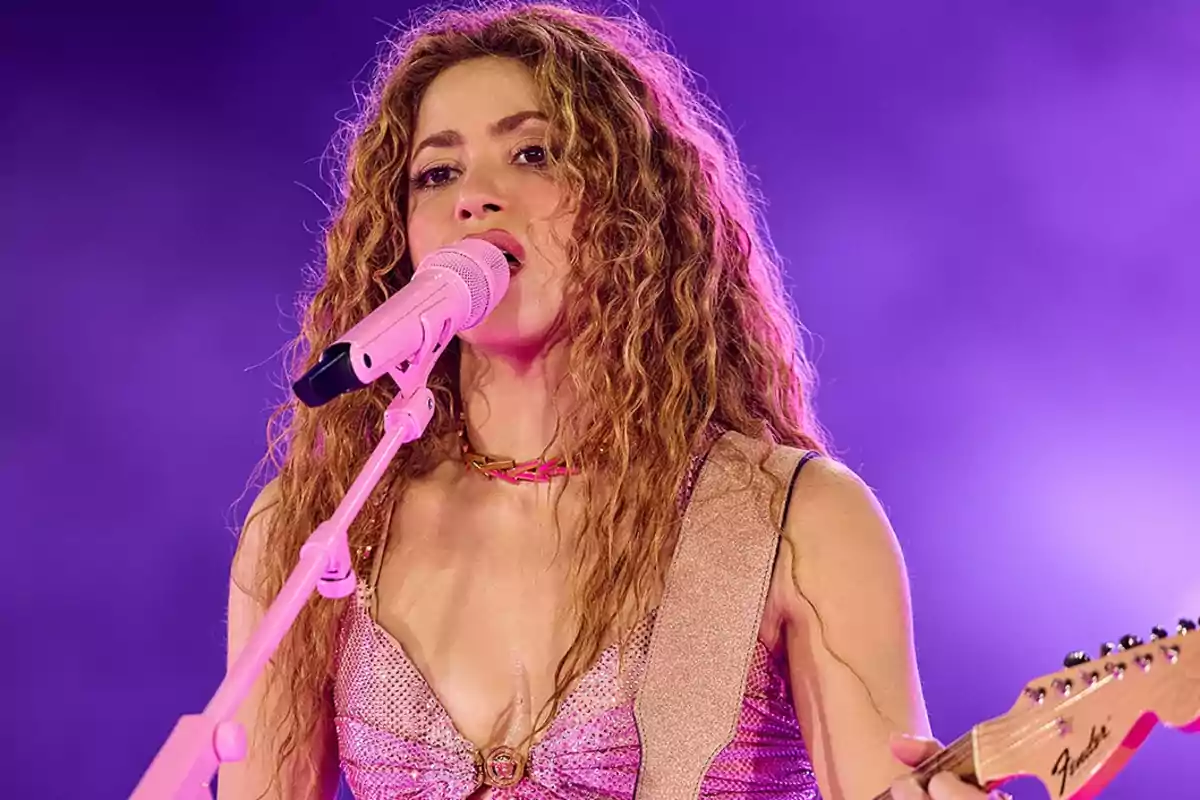 Una persona cantando en un escenario con un micrófono rosa y una guitarra bajo una iluminación púrpura.