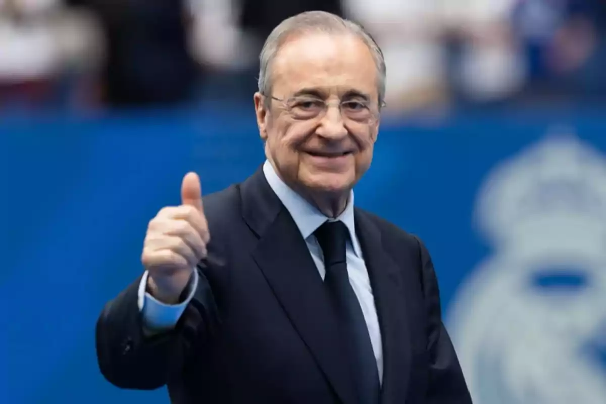 Older man with glasses and a dark suit smiles and gives a thumbs up in approval against a blue background Older man with glasses and a dark suit smiles and gives a thumbs up in approval against a blue background