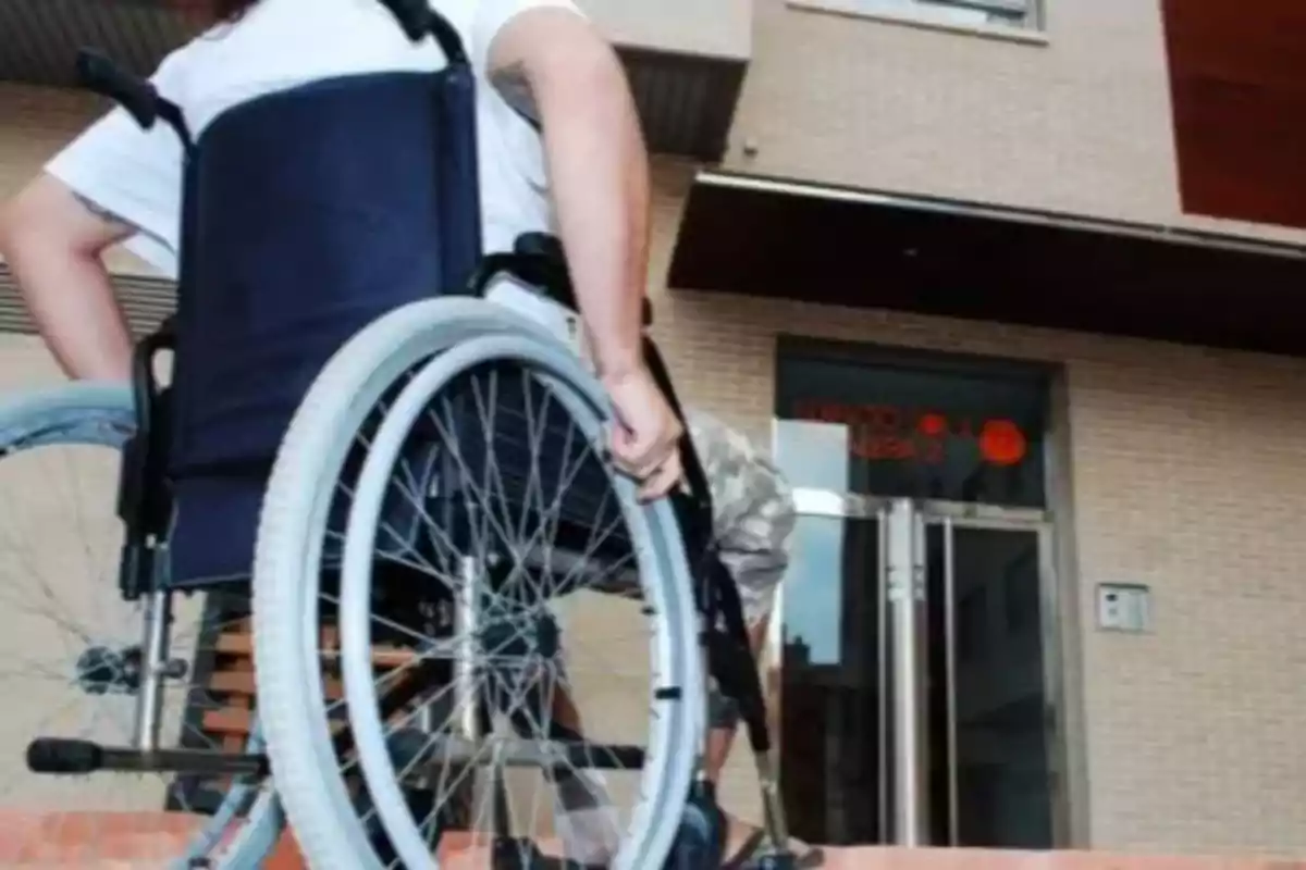 A person in a wheelchair tries to go up a step in front of a building. A person in a wheelchair tries to go up a step in front of a building.