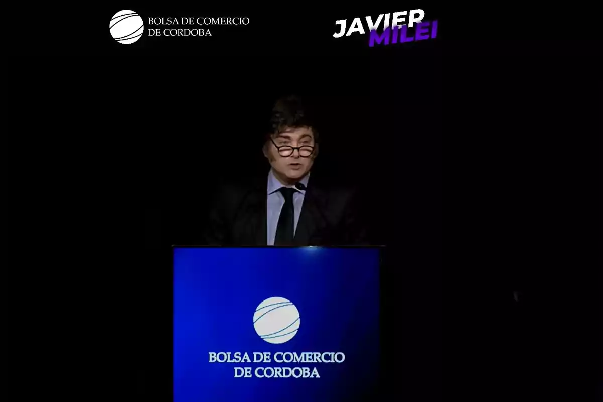 Un hombre con gafas habla en un podio azul con el logo de la Bolsa de Comercio de Córdoba, en un fondo oscuro.