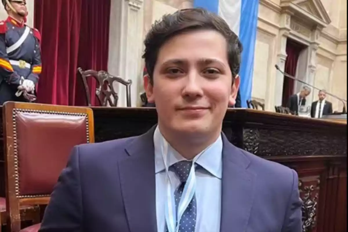 A man in a suit and tie in a formal setting with a flag in the background.