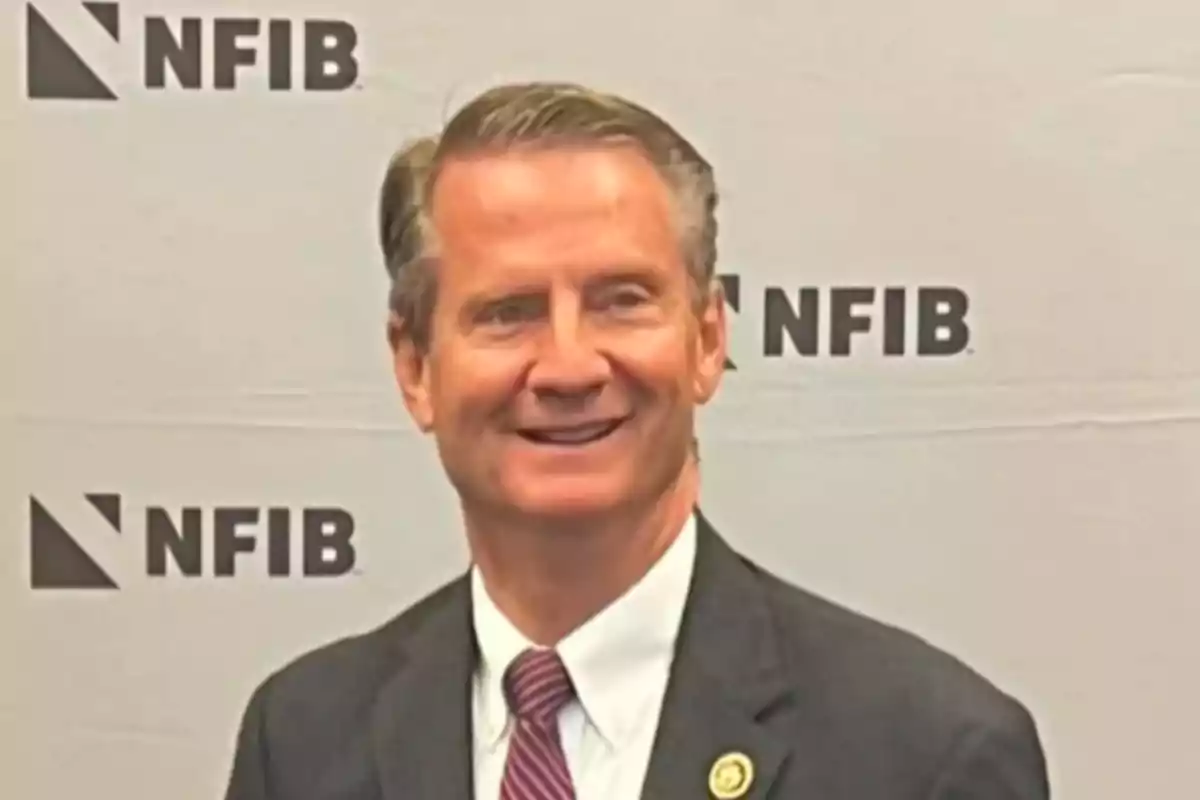 Un hombre sonriente con traje y corbata frente a un fondo con el logotipo de NFIB.