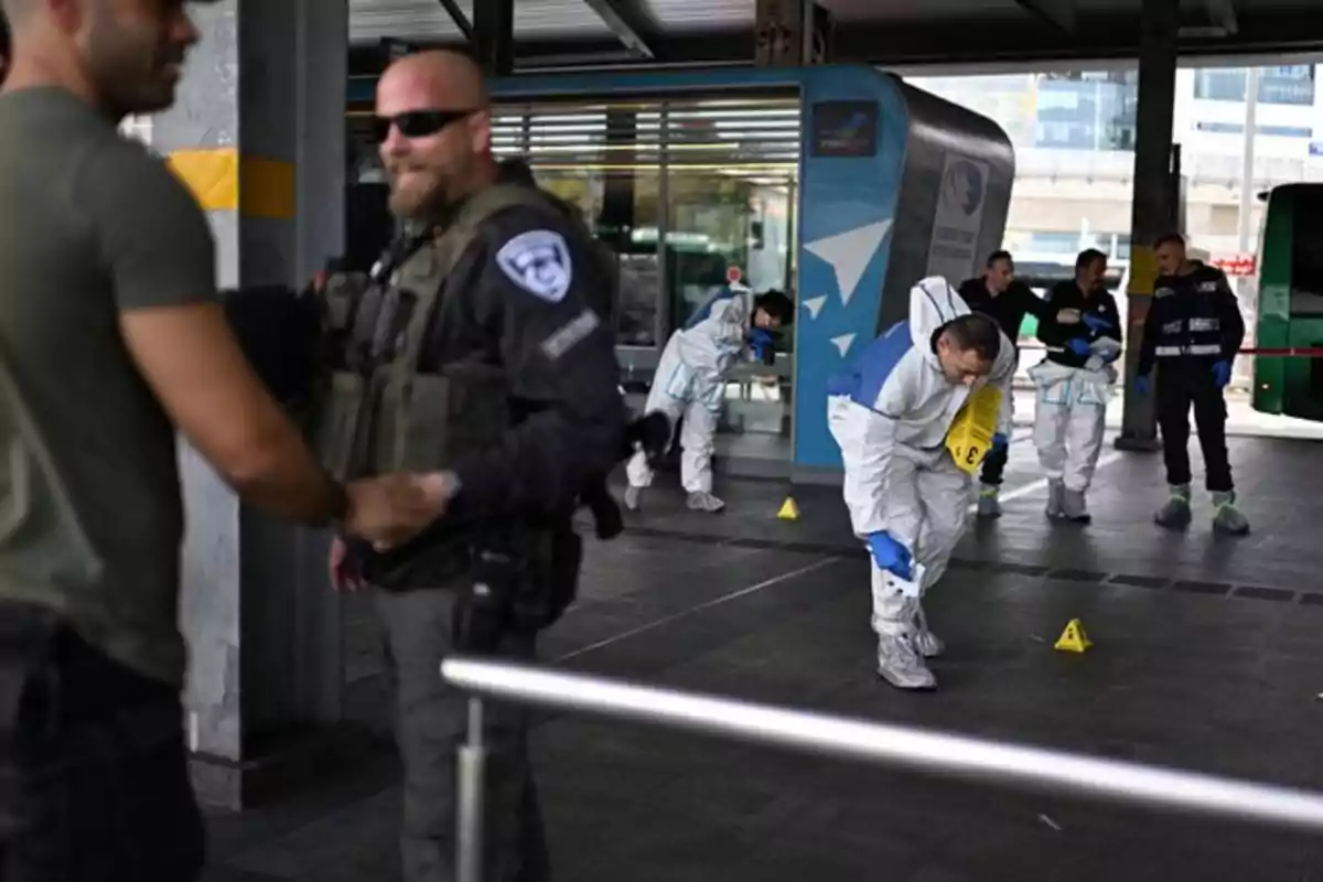 A group of people in protective suits and a security officer are at a transportation station, conducting an investigation at the scene.