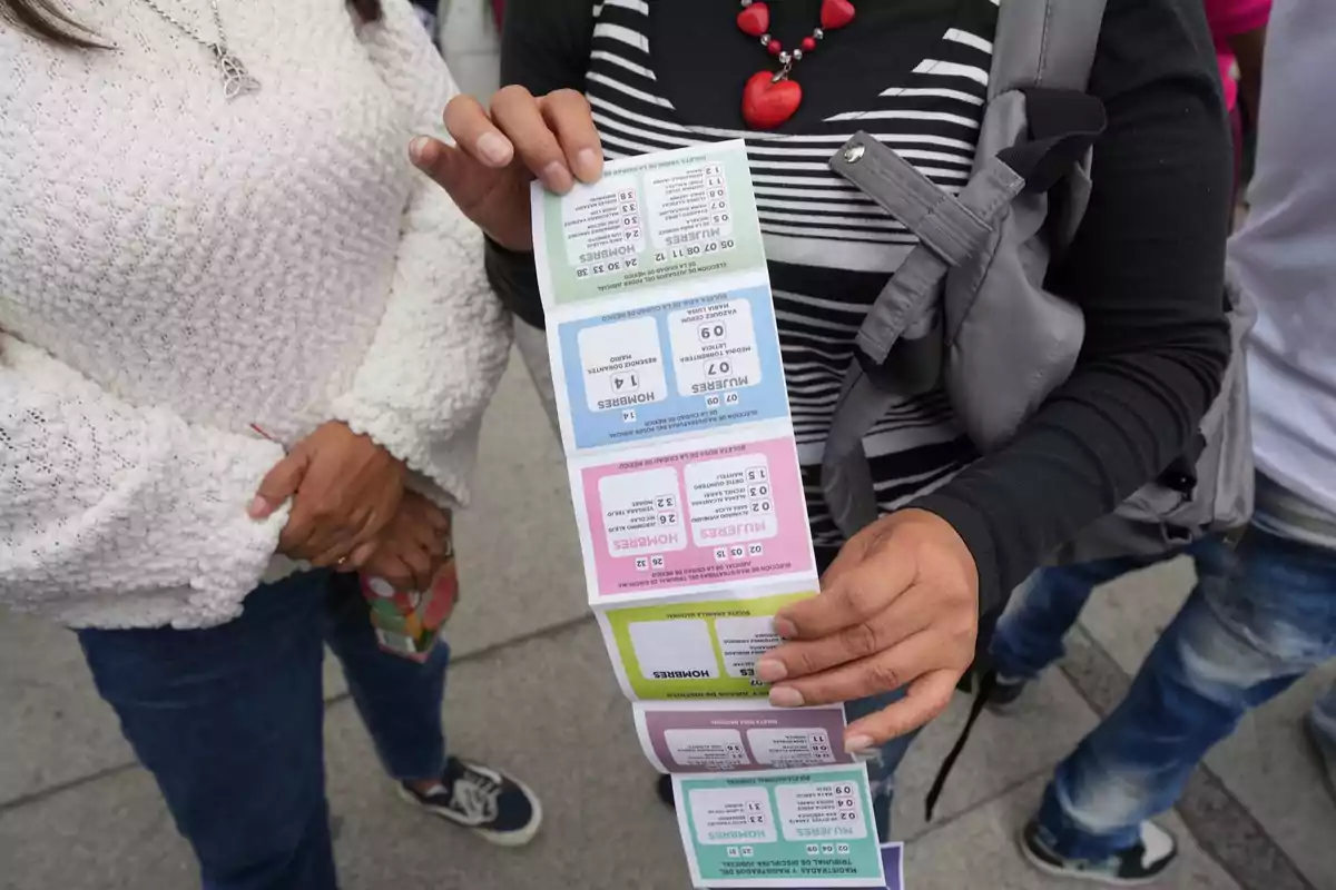 Two people standing on the street, one of them holding a ballot with several sections in different colors. Two people standing on the street, one of them holding a ballot with several sections in different colors.