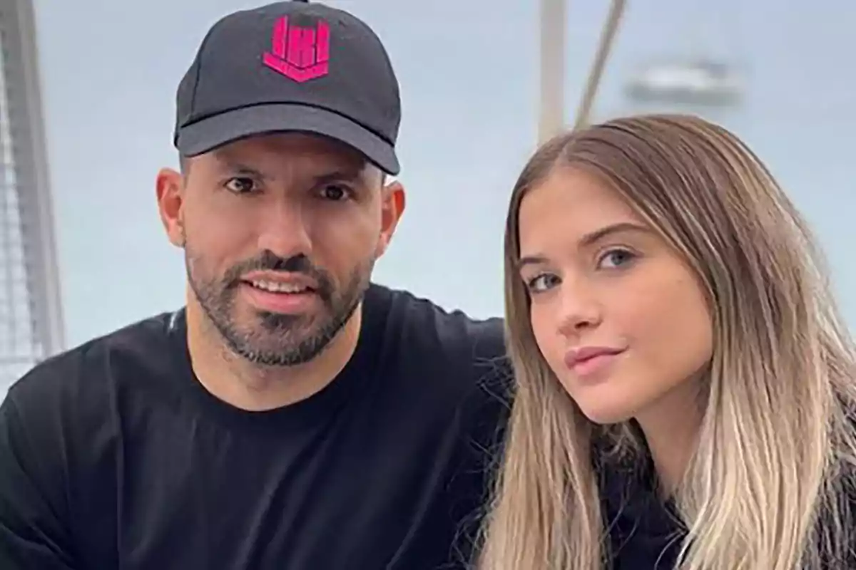 Two people posing together, one of them wearing a black cap with a pink logo. Two people posing together, one of them wearing a black cap with a pink logo.