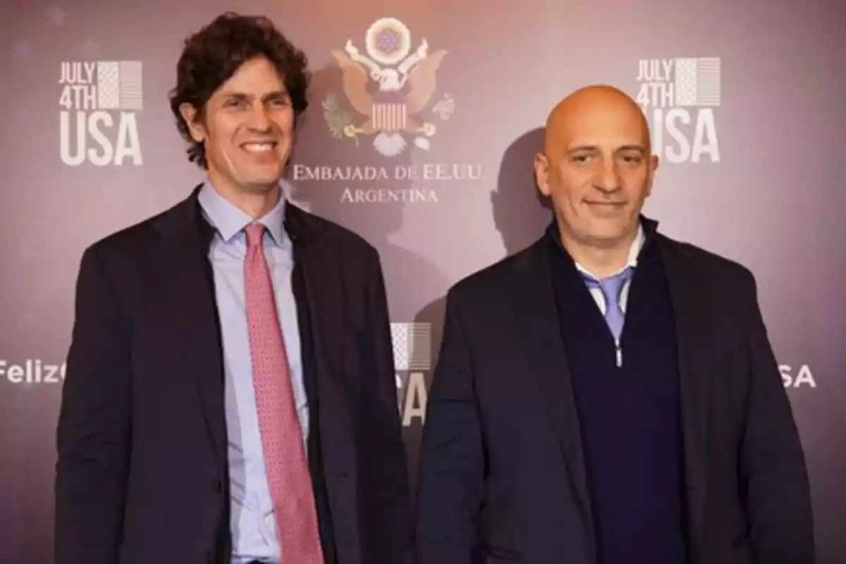 Dos hombres posan frente a un fondo con el logo de la Embajada de EE.UU. en Argentina durante una celebración del 4 de julio.