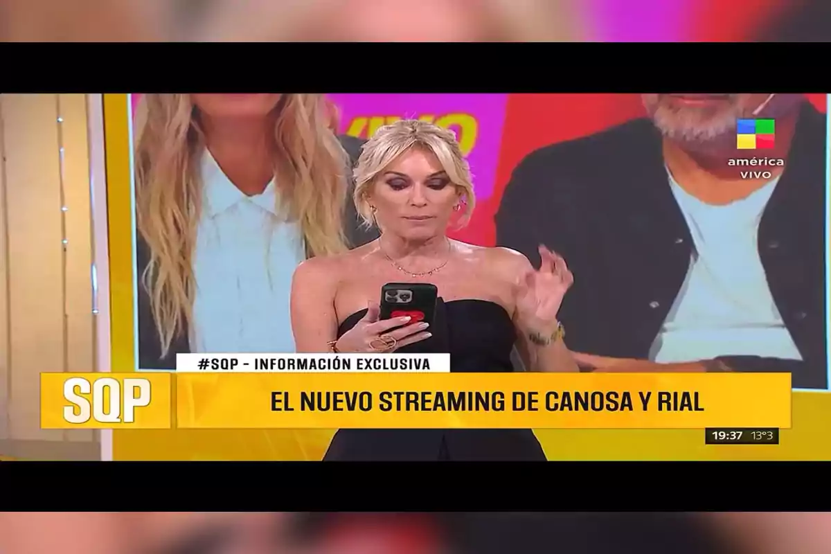 Una conductora de televisión rubia con vestido negro sostiene un celular mientras presenta una noticia sobre el nuevo streaming de Canosa y Rial en un programa llamado SQP, con gráficos amarillos y el logo de América TV en pantalla. Una conductora de televisión rubia con vestido negro sostiene un celular mientras presenta una noticia sobre el nuevo streaming de Canosa y Rial en un programa llamado SQP, con gráficos amarillos y el logo de América TV en pantalla.