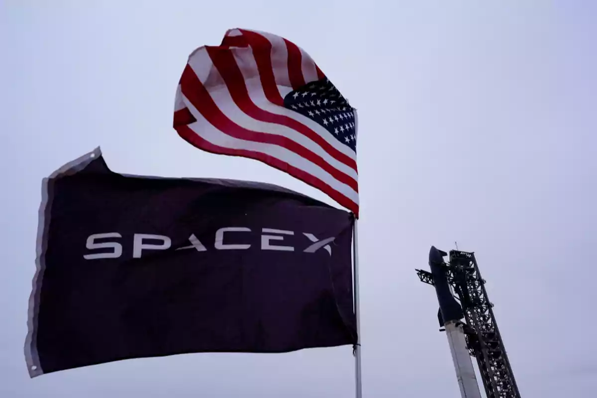 SpaceX and United States flags waving next to a rocket launch pad. SpaceX and United States flags waving next to a rocket launch pad.