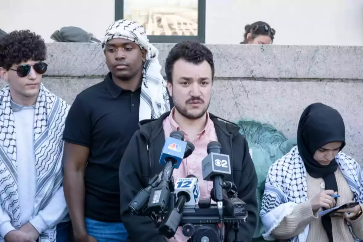 A group of people is gathered in front of a microphone, some of them wearing traditional scarves.