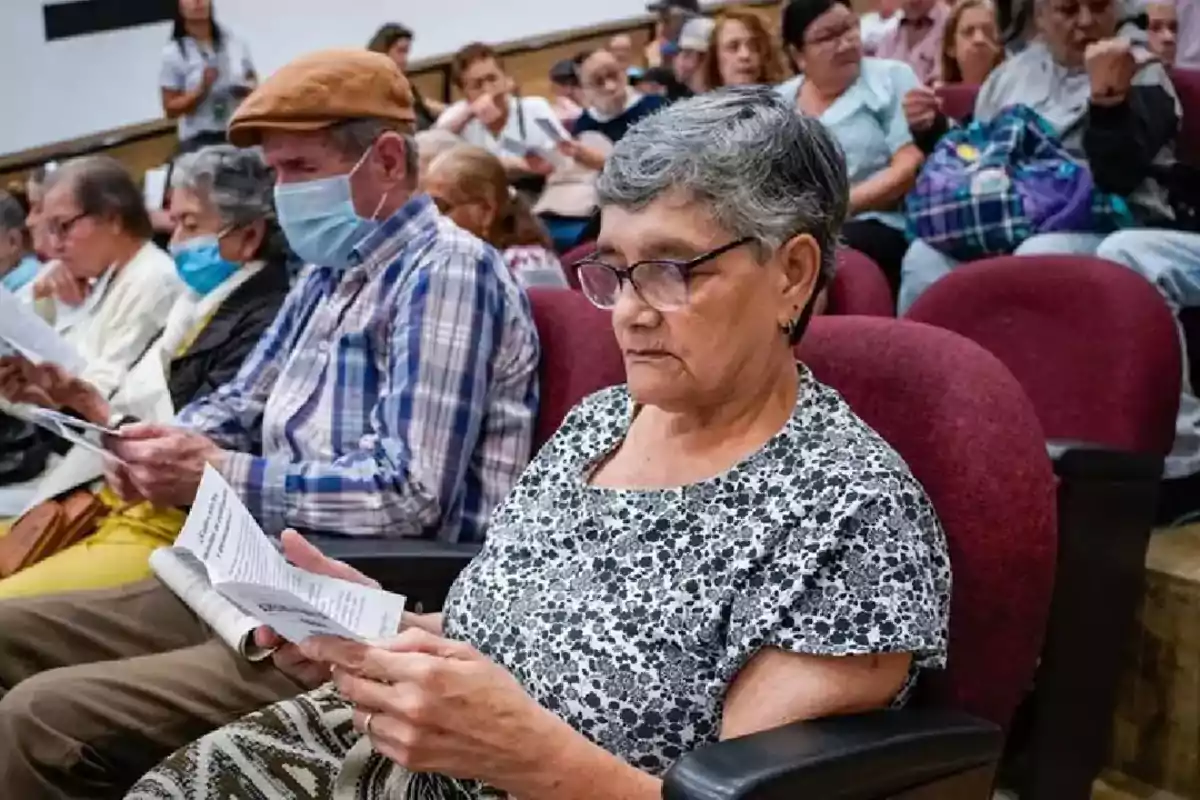 Personas mayores sentadas en un auditorio leyendo documentos.