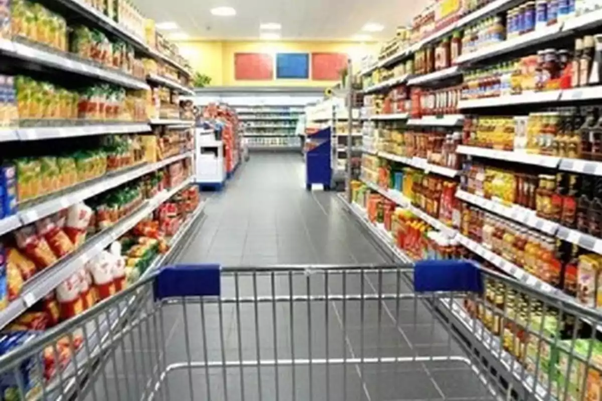 Pasillo de supermercado con estantes llenos de productos y un carrito de compras en primer plano