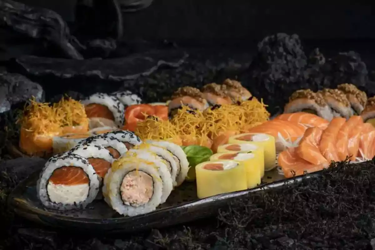 Assorted sushi platter with different types of rolls, nigiri, and salmon sashimi on a dark surface Assorted sushi platter with different types of rolls, nigiri, and salmon sashimi on a dark surface