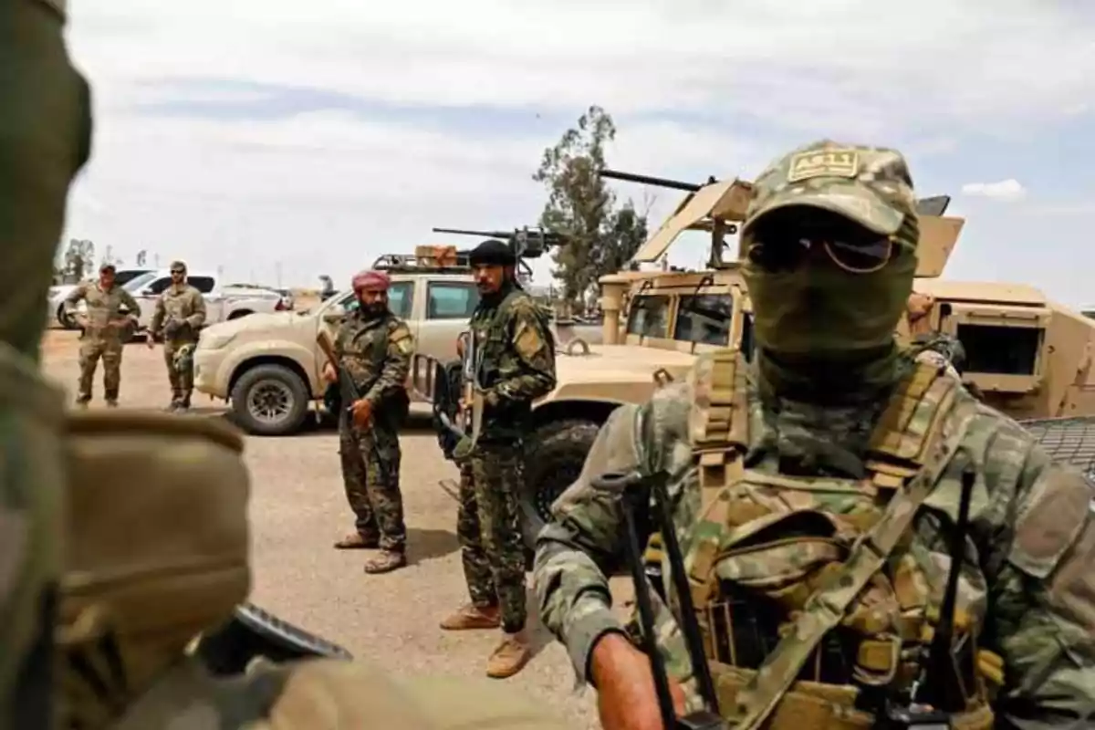 Grupo de soldados en uniforme militar camuflado con vehículos blindados en el fondo.