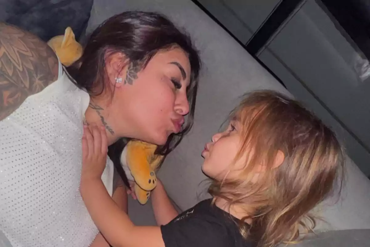 A woman and a girl look closely at each other making a kissing gesture while lying on a couch.