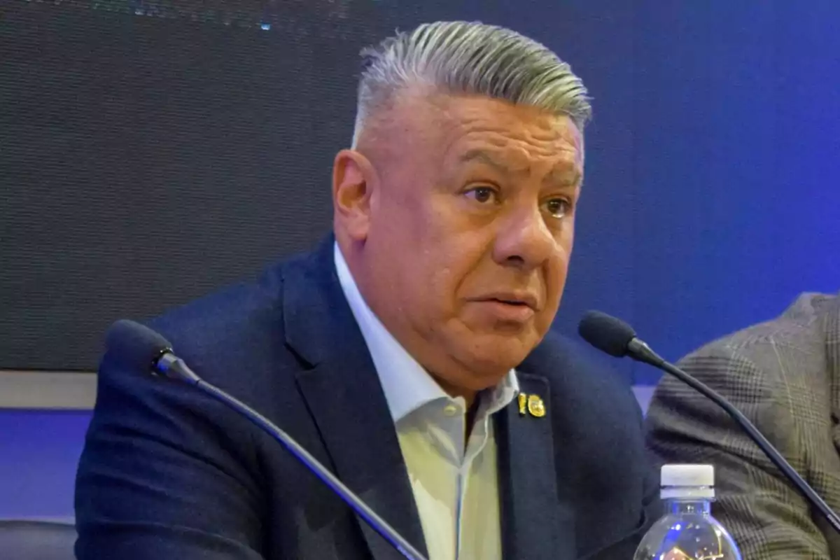 Hombre de cabello canoso en una conferencia de prensa con micrófono y botella de agua. Hombre de cabello canoso en una conferencia de prensa con micrófono y botella de agua.