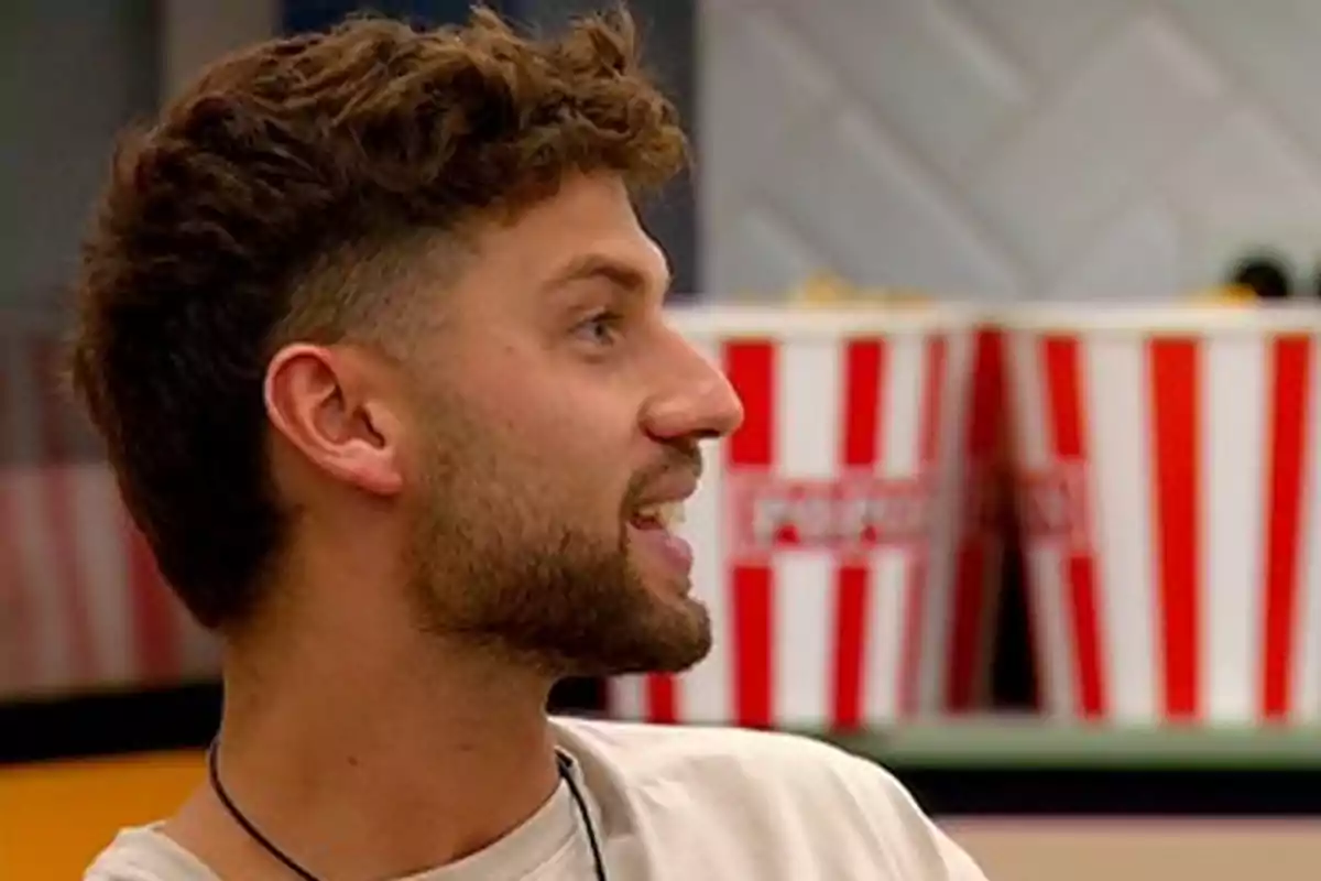 A man in profile with a beard and curly hair in an indoor setting with popcorn boxes in the background. A man in profile with a beard and curly hair in an indoor setting with popcorn boxes in the background.