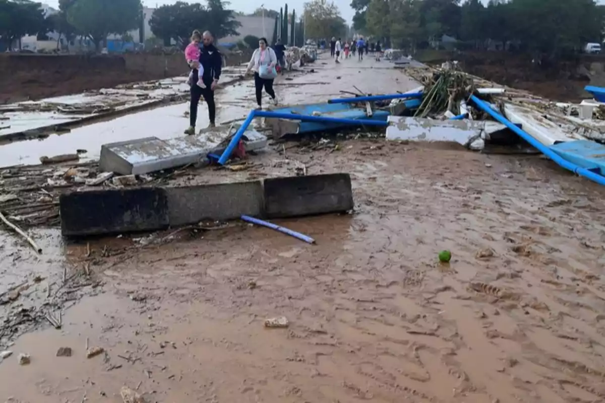 Personas caminando por un camino cubierto de escombros y barro tras una inundación.