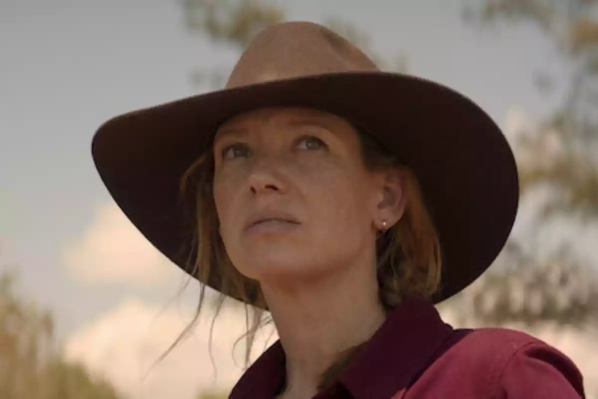 Mujer con sombrero de vaquero mirando hacia el horizonte en un entorno al aire libre.