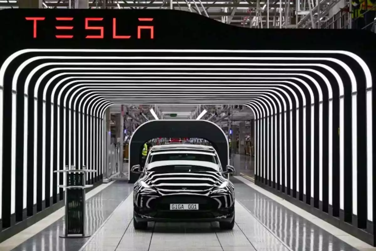 Auto eléctrico Tesla saliendo de una línea de producción en una fábrica moderna con luces blancas y el logo de la marca en la parte superior Auto eléctrico Tesla saliendo de una línea de producción en una fábrica moderna con luces blancas y el logo de la marca en la parte superior