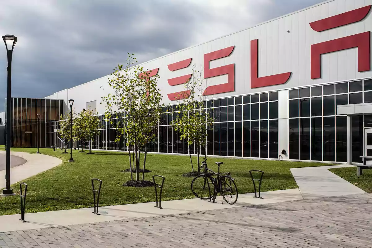 Edificio de Tesla con fachada de vidrio y un área verde con árboles y una bicicleta estacionada.