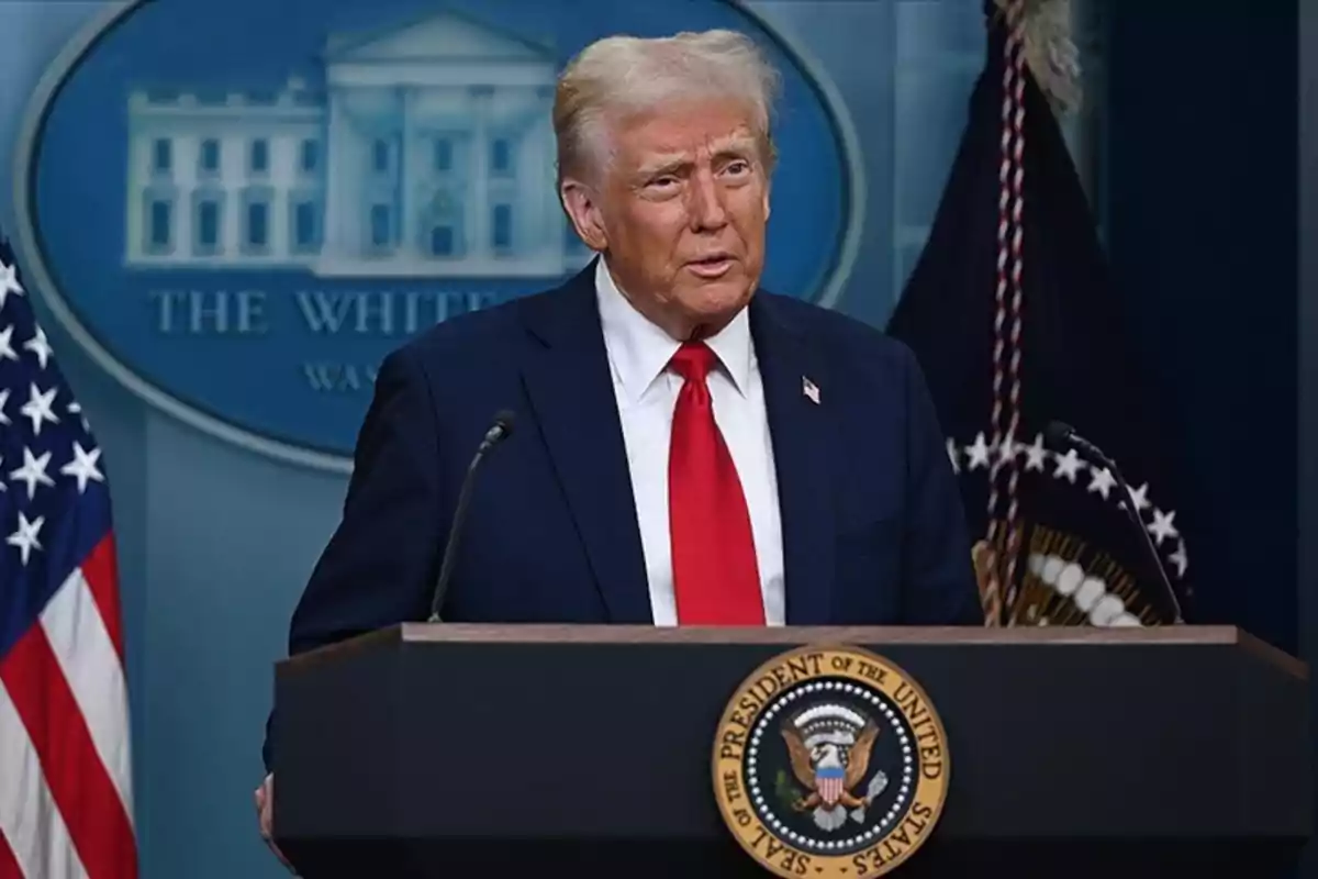 Un hombre de traje oscuro y corbata roja habla desde un podio con el sello presidencial de Estados Unidos, con banderas y el emblema de la Casa Blanca en el fondo.