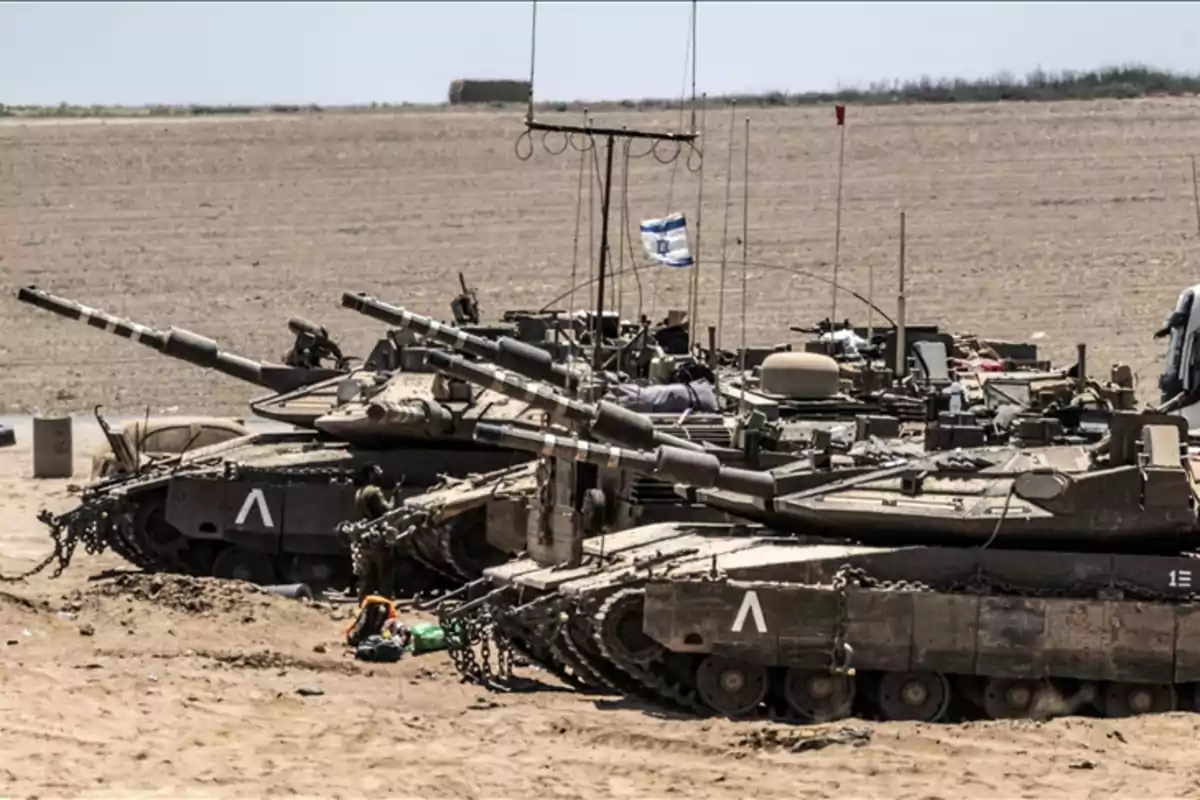 Tanques militares en un terreno arenoso con una bandera ondeando.