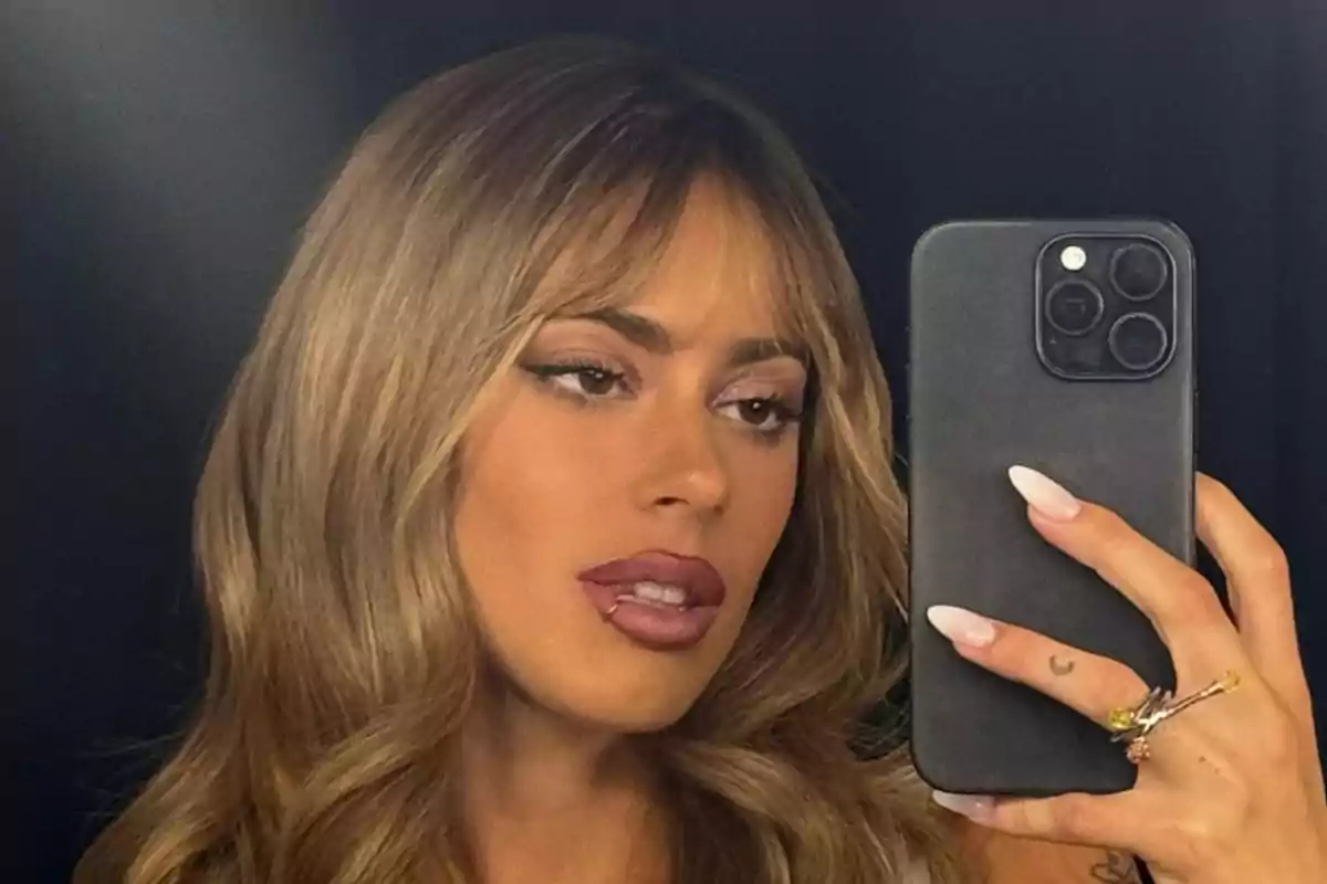 Una persona con cabello rubio y maquillaje toma una selfie con un teléfono móvil.