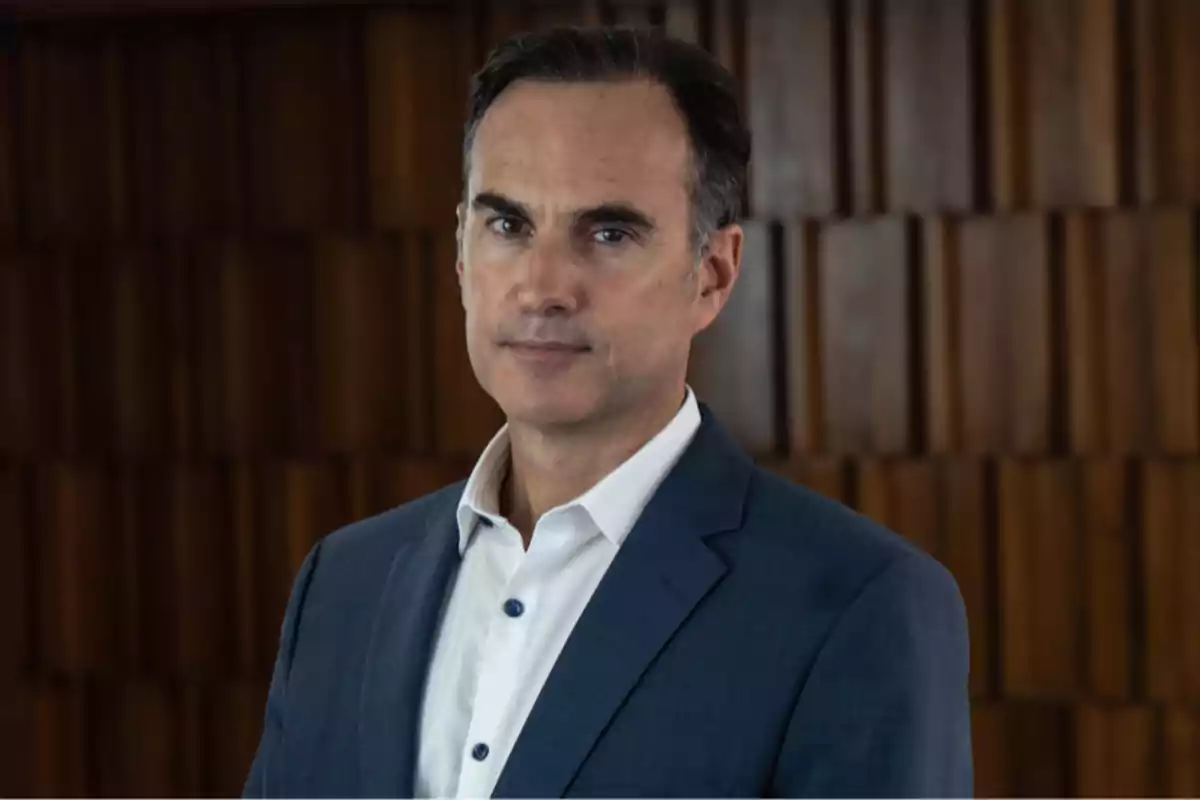 Hombre de traje azul y camisa blanca posando frente a un fondo de madera. Hombre de traje azul y camisa blanca posando frente a un fondo de madera.