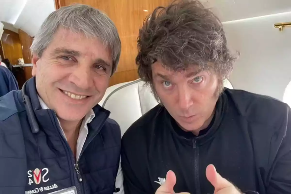 Dos personas posan para una selfie dentro de un avión, una de ellas sonríe mientras la otra hace un gesto con las manos.