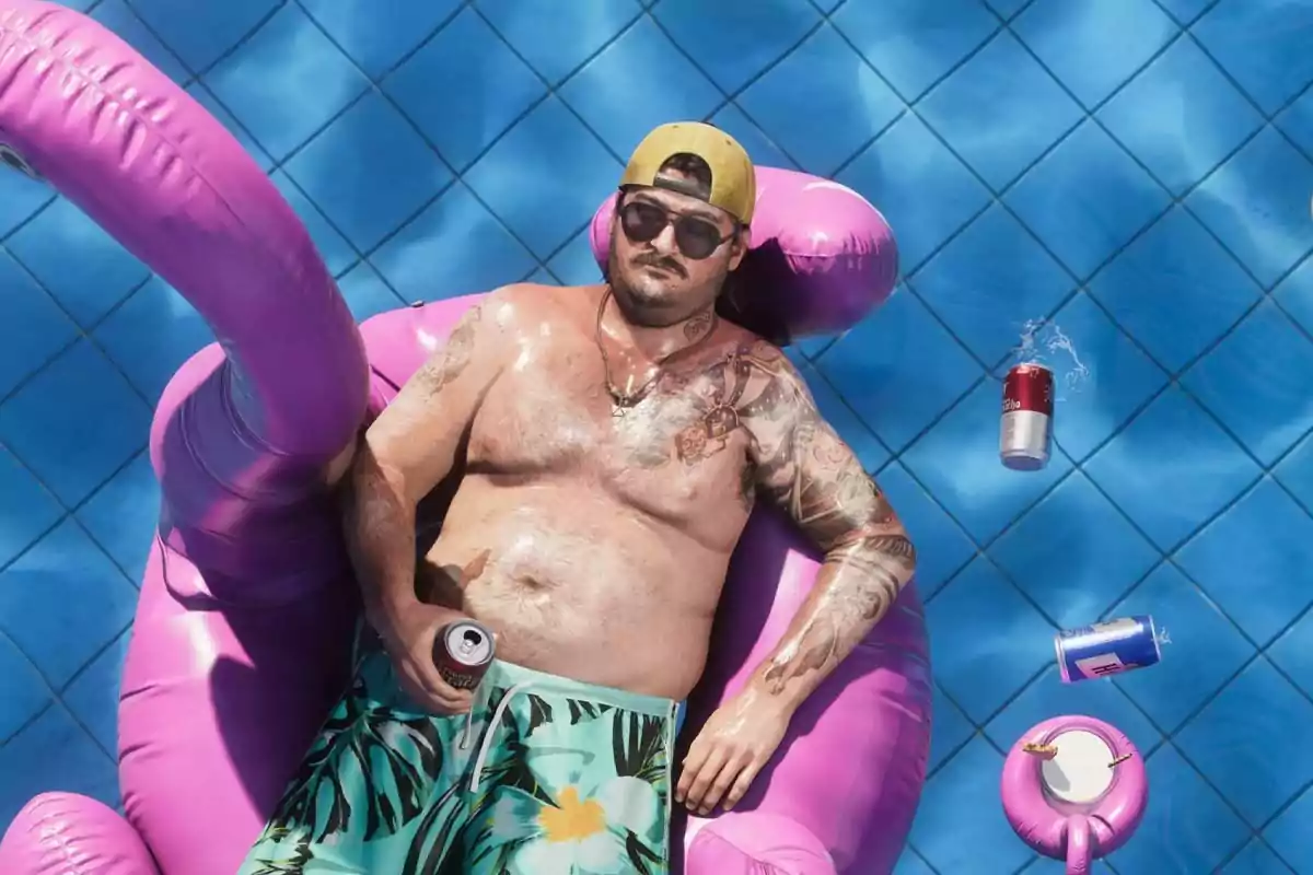 Hombre con tatuajes y gafas de sol descansando en un flotador rosa en una piscina, rodeado de latas de bebida. Hombre con tatuajes y gafas de sol descansando en un flotador rosa en una piscina, rodeado de latas de bebida.