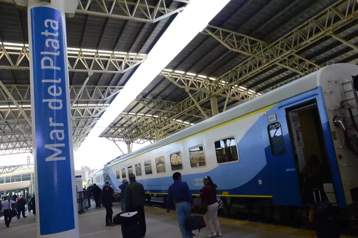 Personas abordando un tren en una estación con un cartel que indica Mar del Plata.