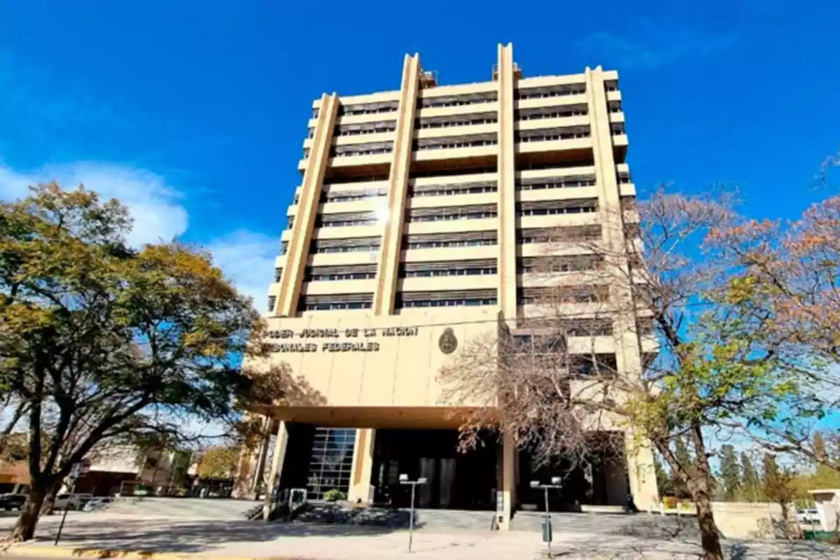 Edificio alto de color beige con varias ventanas y árboles a su alrededor bajo un cielo azul despejado Edificio alto de color beige con varias ventanas y árboles a su alrededor bajo un cielo azul despejado