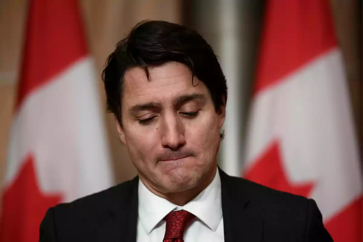 Un hombre con expresión seria y banderas de Canadá al fondo.