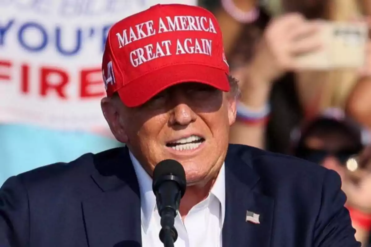 Una persona con gorra roja hablando en un micrófono durante un evento al aire libre.