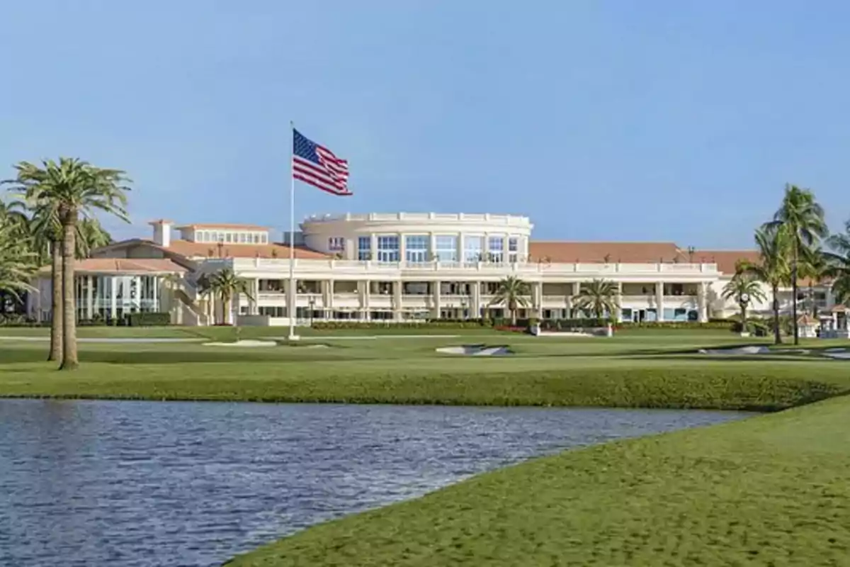 Edificio elegante con una bandera estadounidense ondeando en un campo de golf rodeado de palmeras y un lago.