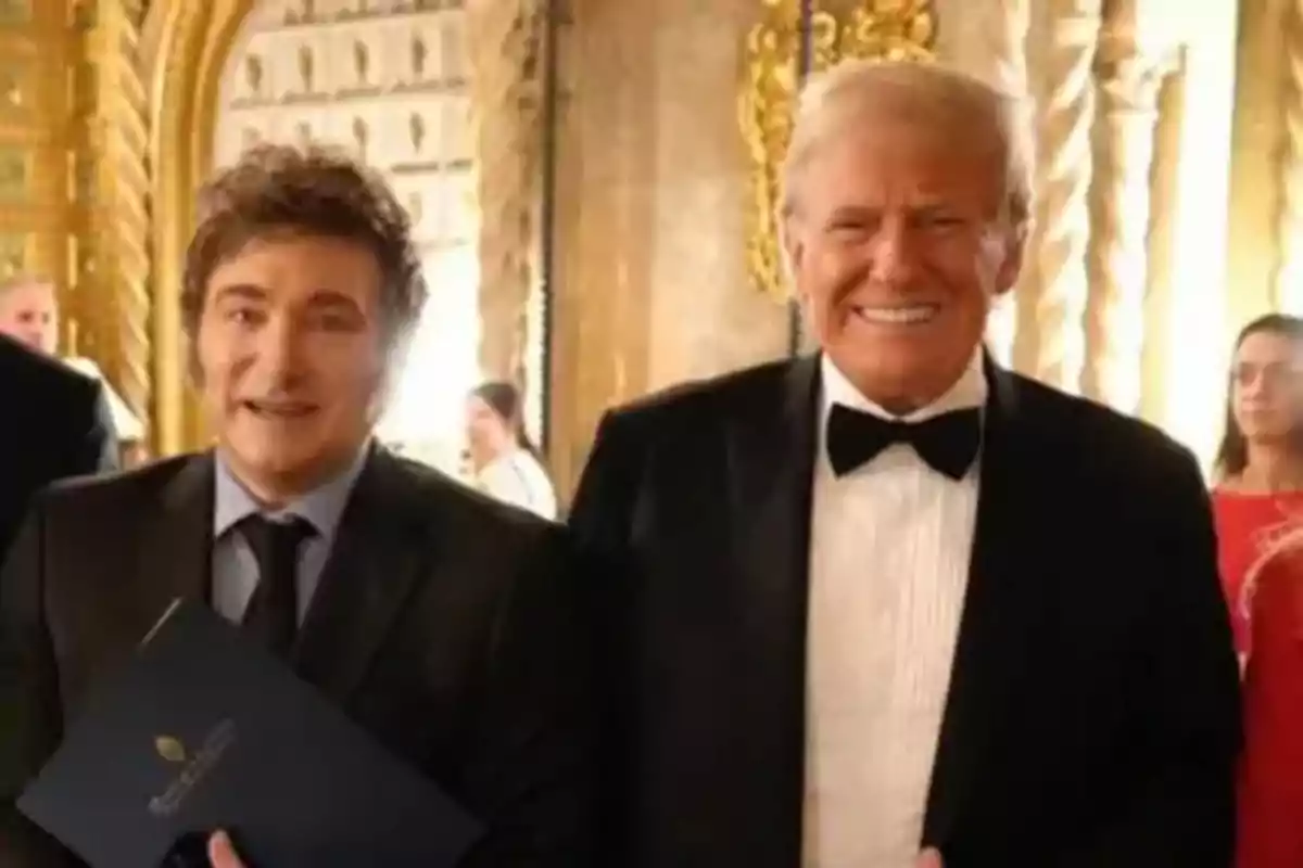 Dos hombres sonrientes vestidos de traje en un elegante salón con decoración dorada.