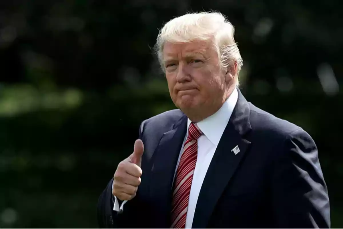 Hombre de cabello rubio con traje oscuro y corbata roja haciendo un gesto de pulgar arriba Hombre de cabello rubio con traje oscuro y corbata roja haciendo un gesto de pulgar arriba