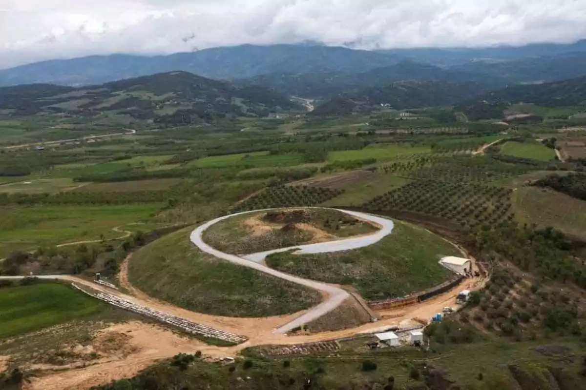Aerial view of a mountainous landscape with a winding road over a hill surrounded by green fields and mountains in the background. Aerial view of a mountainous landscape with a winding road over a hill surrounded by green fields and mountains in the background.