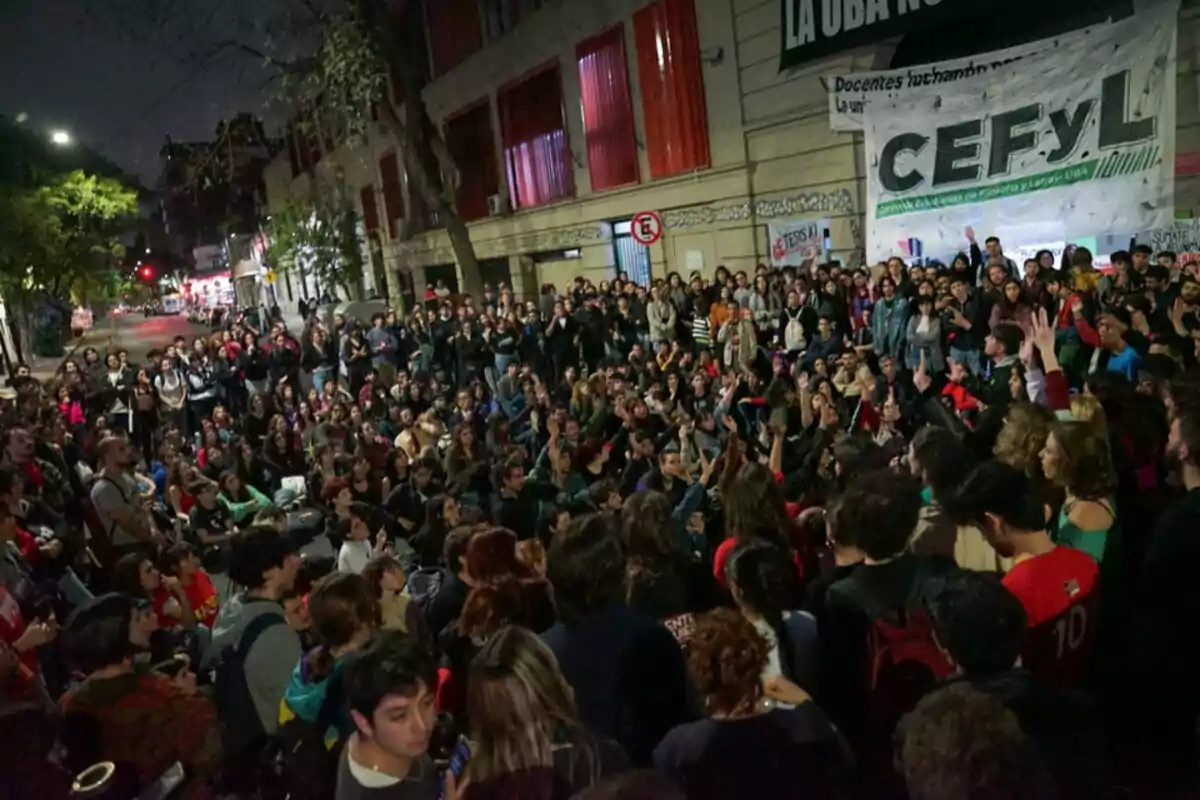 Una multitud de personas reunidas en una calle frente a un edificio con un cartel que dice "CEFYL" durante la noche.