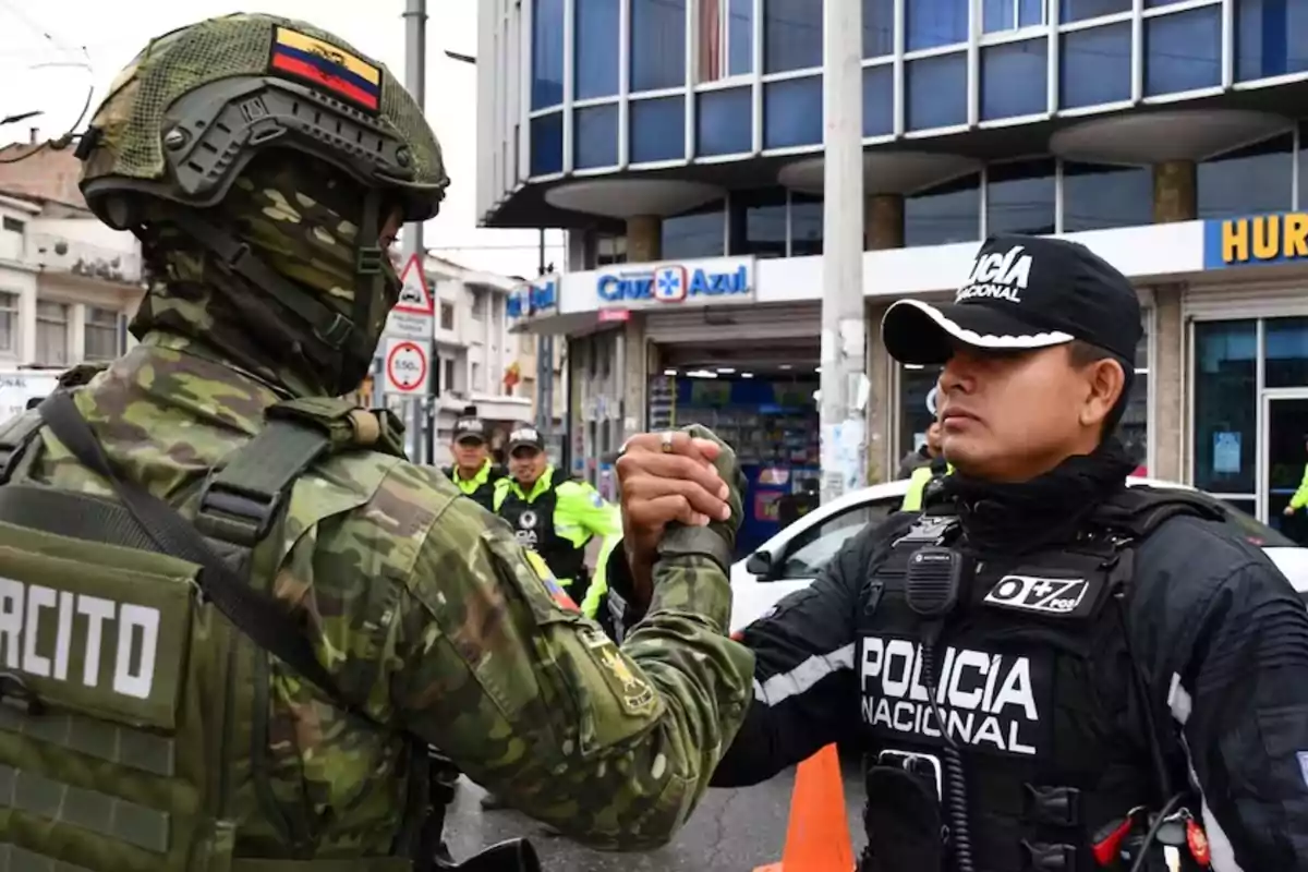 Un soldado y un policía se saludan con un apretón de manos en una calle urbana, con otros oficiales en el fondo.