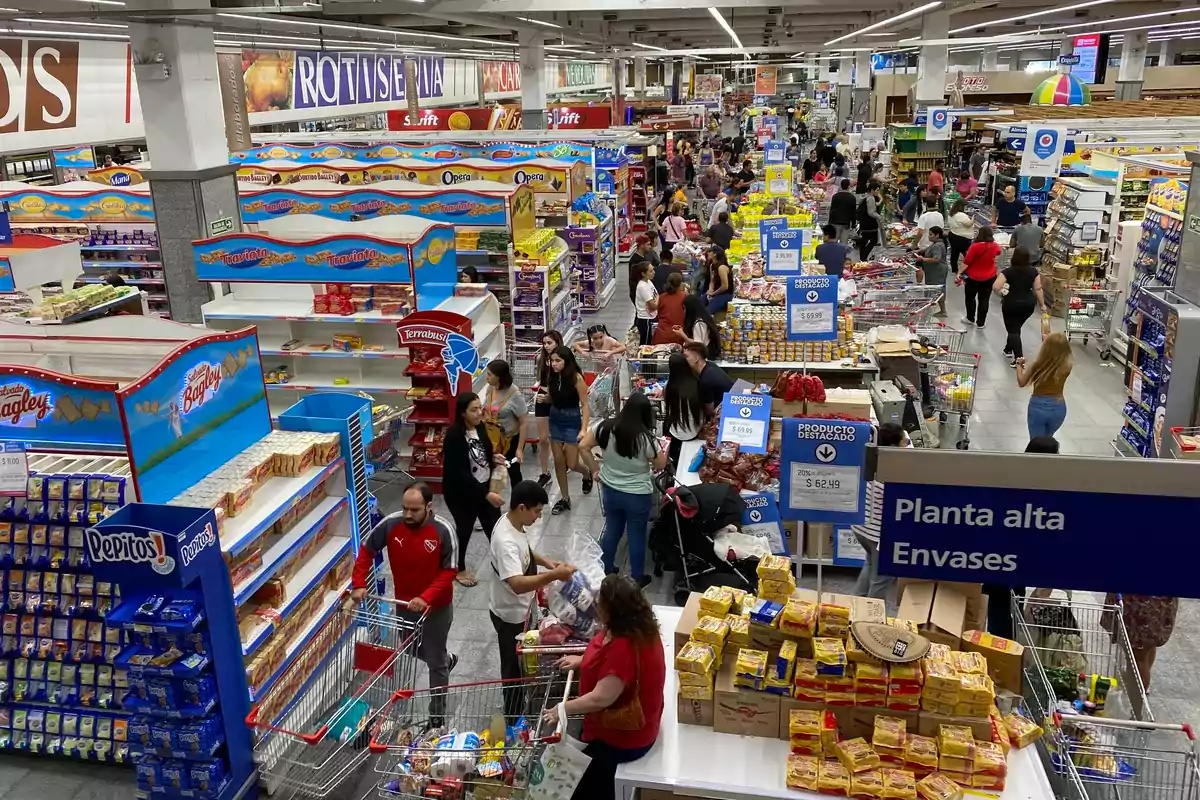 Supermarket full of people shopping with carts among shelves stocked with products and signs for different sections Supermarket full of people shopping with carts among shelves stocked with products and signs for different sections