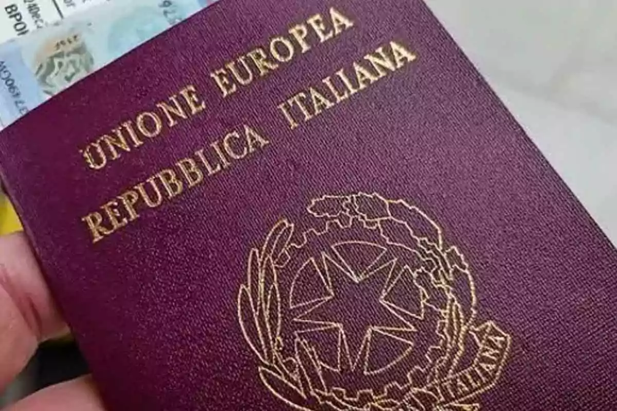 A hand holding an Italian passport with a partially visible document behind it. A hand holding an Italian passport with a partially visible document behind it.
