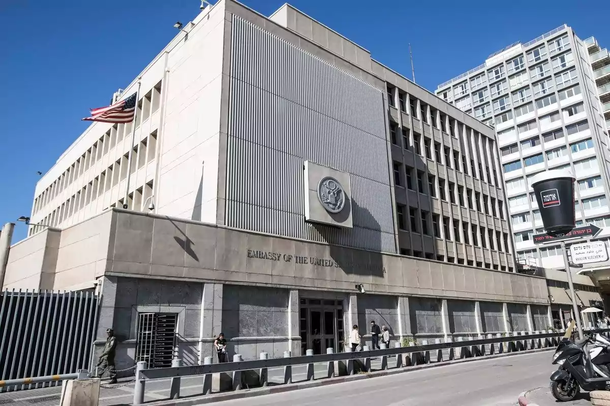 United States embassy building with a waving flag and people at the entrance in a modern city