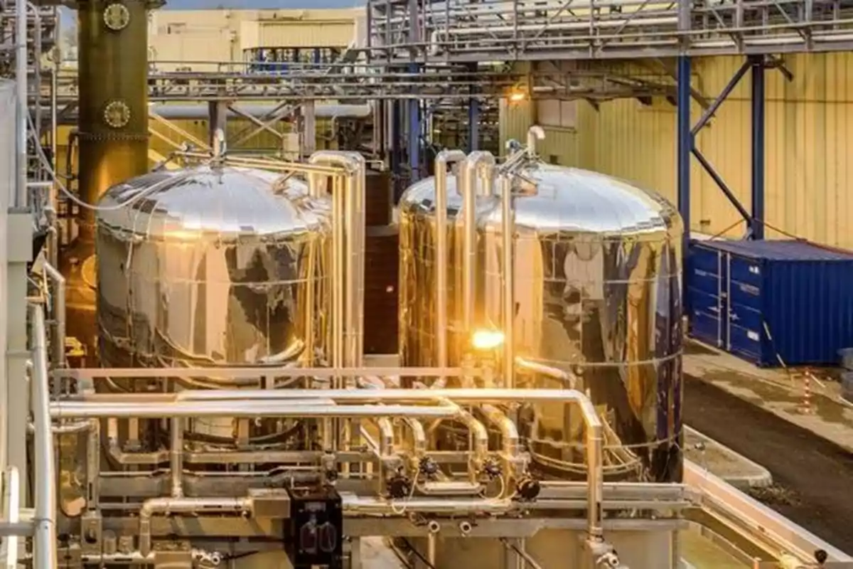 Tanques industriales de acero inoxidable rodeados de tuberías y estructuras metálicas en una planta de procesamiento Tanques industriales de acero inoxidable rodeados de tuberías y estructuras metálicas en una planta de procesamiento
